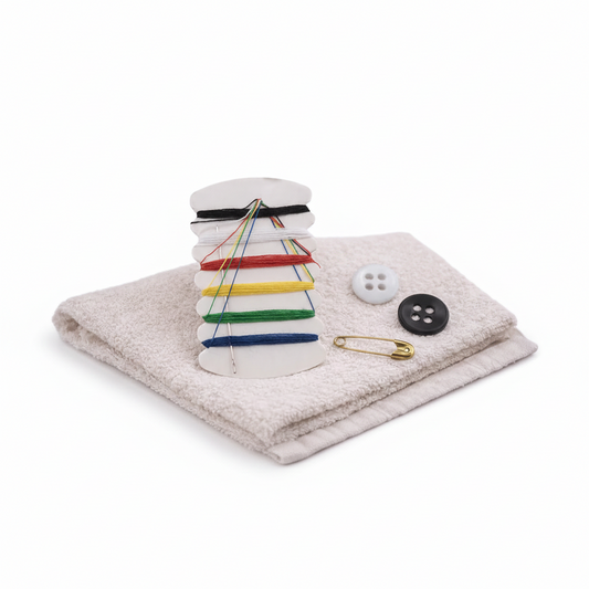 Stack of folded towels with colorful pins, a button, and safety pin on a towel with candles in the background.